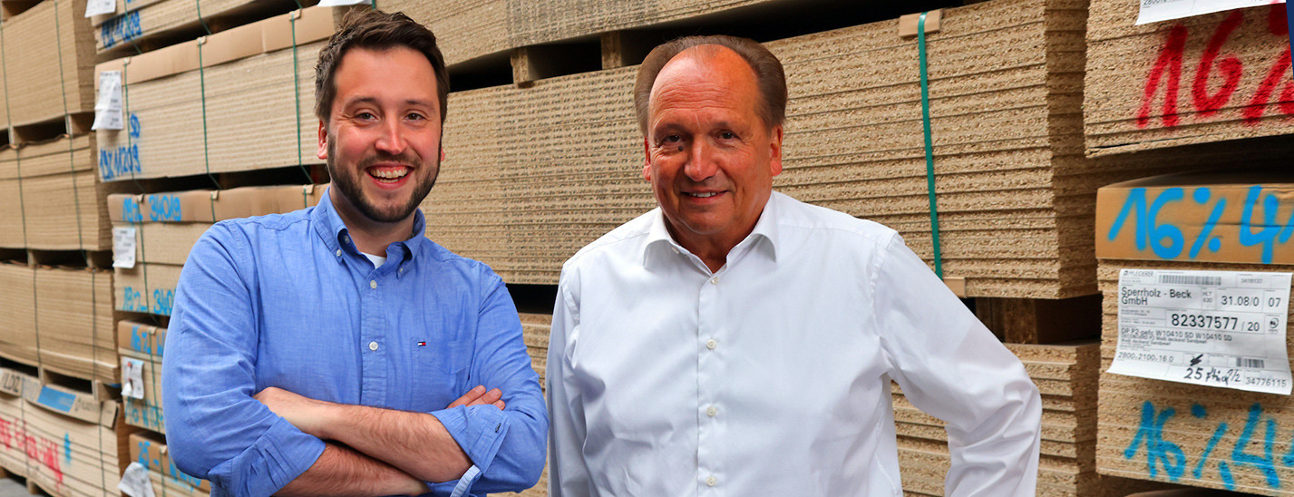 Die Geschäftsführer Heinz und Marc Oliver Junker vor einem Stapel Holzplatten im Lager
