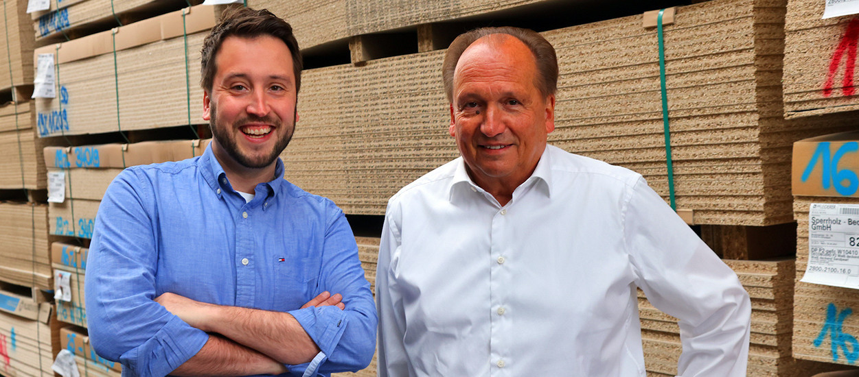 Die Geschäftsführer Heinz und Marc Oliver Junker vor einem Stapel Holzplatten im Lager
